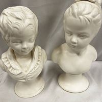 Front view of both vintage Lefton bisque porcelain bust statues showing Victorian boy and girl.