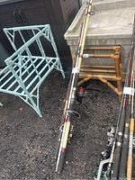 Fishing rods leaning against light blue and brown chairs on ground outside.