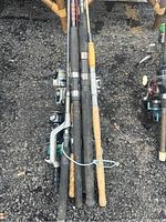 Top view of the bundled fishing rods with reels on black gravel ground showing foam and cork handles.