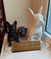 Photo showing two ceramic dog figurines (one black, one white), one dark blue ceramic pig figurine, two clear glass pig salt and pepper shakers, and a gold-colored metal sign.