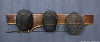 Front view of wooden plaque displaying three vintage fencing masks mounted horizontally with an epee below.
