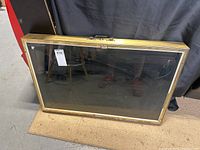 Full view of rectangular display case with brass-colored metal frame and glass front, standing upright on carpet.