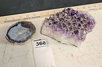 Photo showing two geodes on a table with a measuring ruler; one is a round geode with grayish-blue and brown tones, the other a larger amethyst quartz cluster with purple crystals.