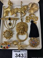 Full set of nine gold-tone rhinestone brooches and a lion head pendant with a ring in the mouth, displayed in a white box.