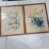 Pair of framed botanical flower prints, one with pastel pink and cream flowers and the other with yellow and blue flowers. Both signed B. Riasni.