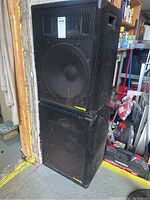 Two black Community brand DJ speakers stacked on each other in a storage area, showing exterior cabinet and grille condition.