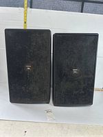 Front view of the pair of black JBL outdoor speakers showing the metal grills with dust and wear.