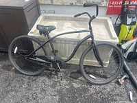 Full side view of black Schwinn beach cruiser bike showing frame, seat, handlebars, tires, and pedals on asphalt surface.