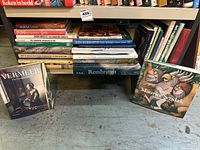 Shelf filled with a variety of art books and illustrated books, including prominent titles such as Vermeer The Complete Paintings, Rembrandt, and The Art of Maurice Sendak, displayed on a concrete floor.