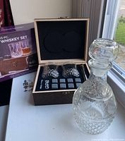 Full whiskey set displayed with wooden box open showing contents and glass decanter beside it.