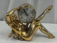 Full view of the gold-tone nude female figurine holding the clock face.