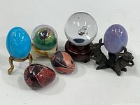 Full view of all miniature eggs and globes including two soapstone eggs, three ceramic eggs on stands, plastic bug globe and clear glass globe on wood stand.