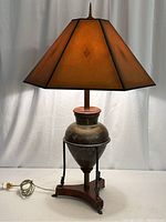 Full view of sculptured lamp showing copper metal body, wood base, black metal frame, and hexagonal paper shade.