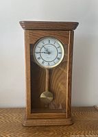 Front view of the 23 inch Linden Westminster Quartz Pendulum Clock showing the wooden case, round clock face with Roman numerals, and visible brass pendulum.