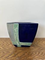 Square-shaped blue flower pot planter with green stripes, showing front view on a wooden surface with neutral background.