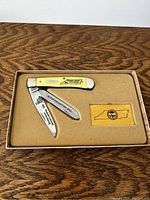 Top-down view of vintage folding pocket knife with yellow handle and three blades, displayed in open box with felt lining.