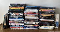 Large stacks of assorted BluRay and DVD movies arranged in multiple rows, showing a variety of titles including Star Wars, Avatar, Happy Feet, Super 8, and others.