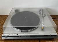 JVC L-A31 turntable with dust cover, showing the front and top view of the turntable and tonearm, on a wood surface.
