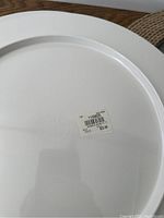 Back of a large white charger plate showing embossed marking and barcode sticker.