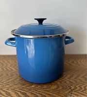 Blue enamel coated carbon steel stock pot with lid, shown standing on wood surface.
