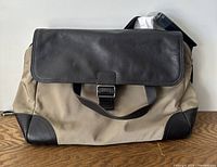 Front view of the vintage Banana Republic messenger bag showing beige canvas and dark brown leather flap, corners, and buckle strap, placed on a wooden surface