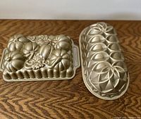 Two baking pans on wood surface, one square with pumpkin motifs and one oval bundt cake pan with geometric, star-shaped segments