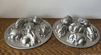 Photo showing two round aluminum baking pans with six 3D bunny shapes each, detailed with varying poses and fur textures.