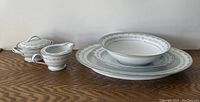 Full set arranged on wood surface showing covered sugar bowl, creamer, and three plates (soup, salad, and dinner) with delicate silver-gray scrollwork trim