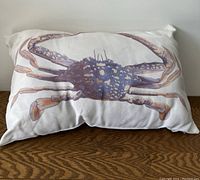 Front view of the rectangular pillow with a king crab printed on white fabric, placed on a wooden surface.