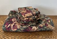 Folded floral tablecloth with six napkins stacked on top, showing the full pattern and texture.