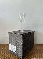 Wine glass shown placed on top of a black geometric patterned box with label on the side.
