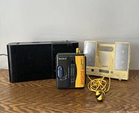 Photo showing a vintage Sony Sports Walkman, yellow earbuds, and two portable speakers (black and cream-colored).