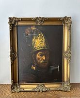 Full view of the framed oil painting depicting a man wearing a golden gilt helmet, dark background, detailed face and helmet features, hanging on a white wall.