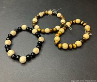 Three beaded bracelets on black surface showing wood beads and black and tiger's eye stone beads