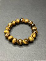 Image showing the elastic bracelet made of polished tiger's eye gemstone beads arranged in a circular shape on a dark surface.