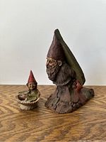 Large and small Tom Clark gnome figurines side by side on wood surface, showing detailed features and paint.