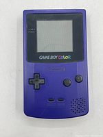 Front view of purple Nintendo Game Boy Color handheld console showing screen, power light indicator, directional pad, A and B buttons, and Select and Start buttons.