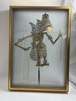 Full front view of the gilt-framed Indonesian shadow puppet showing the entire puppet in the frame.