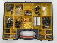 Top view of organizer case with assorted vintage hardware including capacitors, rotary switches, wiring, power plugs, and connectors separated into multiple yellow compartments.