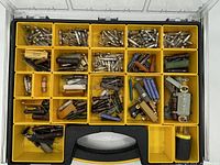 Top view of the open organizer showing multiple yellow compartments filled with assorted vintage hardware items including different types of fuses, screws, metal parts, and electrical components.