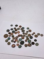 Overview of approximately 50 assorted Roman coins laid out on white background showing various sizes and oxidation levels.