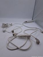 Photo showing multiple white extension cables and power bars laid out, cords visible with three-prong plugs.