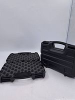 Pair of black hard plastic cases, one closed with handle up, one open showing egg crate foam interior for protection.