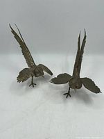 Pair of metal pheasant sculptures viewed from front and side showing wing and tail details.