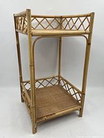 Front angle view of the two-tier rattan side table showing woven rattan shelves and lattice sides.