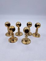 Set of five brass curtain rod holders arranged on white background, showing spherical rod holder ends and round mounting bases with three screw holes each.