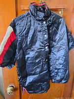 Black satin jacket with colored stripes on sleeve hanging on door