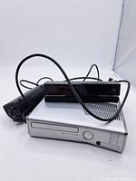 Overall view of silver Xbox 360 console, black Kinect sensor, and power cable laid together