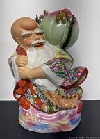 Front view showing smiling elderly figure with white beard and colorful robes holding large peach