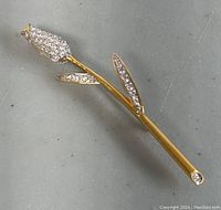 Close up photo of one gold-tone metal rose brooch with clear rhinestones on flower petals and leaves.